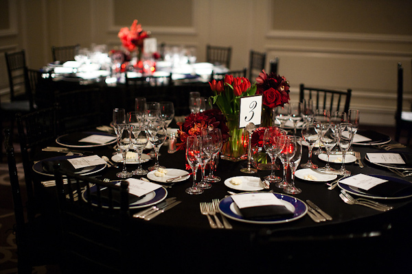 Reception seating - Black tablecloth, dark blue and white dinner plates, and red and green floral centerpiece - wedding photo by Michael Norwood Photography